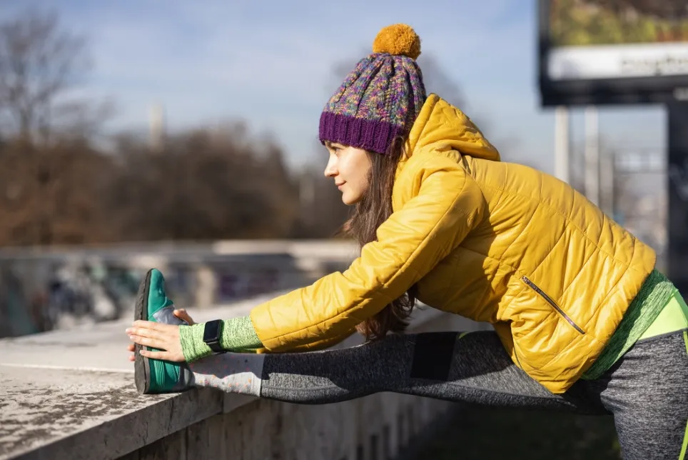 A woman in cold-weather clothing stretching before a run
